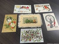 Overview of six vintage greeting postcards arranged flat on surface showing different holiday scenes and messages.