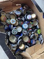 Close-up view of a large quantity of assorted vintage Canadian beer bottle caps inside a cardboard box showing various colorful logos and designs.