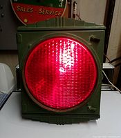 Front view of the green metal traffic stop light with lit red glass lens showing art deco design.