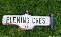 Front view of double-sided Fleming Cres street sign with cast iron frame and crown, showing the text 'FLEMING CRES 73'