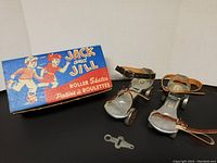 Original pair of Jack and Jill adjustable metal roller skates with leather straps and four wheels each, shown alongside original box and adjustment key.