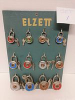 Front view of green Elzett store display board holding 12 padlocks with keys attached.