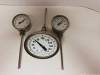 Front view of three Ashcroft industrial thermometers with metal probes and clear glass lenses on white background.