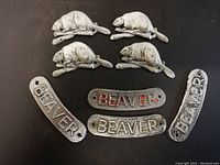 Top down photo of eight metal name plates from Beaver Gumball machines, four shaped like beavers and four rectangular with BEAVER text.