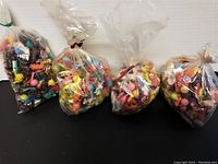 Four bags filled with assorted small colorful plastic toys for vending machines or party grab bags.