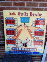 Front view of colorful Bally Strike Bowler back glass panel showing bowling lane, pins, six player score windows, and game scoring text on yellow plexiglass.
