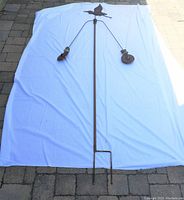 Full view of the weather vane laid on a white sheet outdoors. Shows overall length and forked base for ground installation.