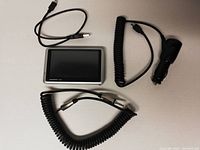 Top down view of Garmin nüvi GPS with all included accessories: coiled car charger, USB cable, and 3.5mm auxiliary audio cable