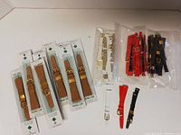 Photo showing packaging of new brown woven leather watch bands and loose white, red, and black leather watch bands in sealed bags.