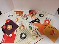Top-down view of 20 assorted 45 RPM vinyl records in original sleeves from different labels including CBS, PolyGram, RCA, and others.