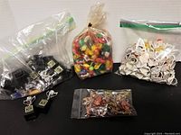Photo showing five groupings of mixed new old stock toys and keychains on a flat surface, including black cube keychains, colorful plastic figurines, white plastic ring toys, and assorted small metal charms.