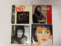 Front view of four 45 RPM vinyl records with original picture sleeves. Included are two Michael Jackson records, one with a group photo and 'Bad' in red text, one with a black and white portrait, plus a Wham! record with colorful sleeve.