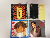 Four 45 RPM records with original picture sleeves front view showing artist artwork and titles: Glass Tiger Thin Red Line, Julian Lennon Valotte, Wham!, Lisa Dal Bello.
