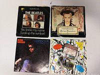 Four 45 RPM records with original picture sleeves laid out showing front sides; includes The Beatles, Culture Club, Bob Seger, and Elvis Costello compilation records.