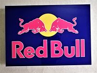 Front view of Red Bull light-up sign unlit, showing logo and text clearly on deep blue background.