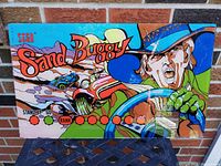 Front side of SEGA Sand Buggy arcade game back glass with colorful artwork, vintage style driver, and vehicle in desert scene.