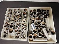 Two trays filled with approximately 102 metal sockets in various imperial and metric sizes, showing some wear from use.
