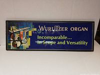 Original Wurlitzer Organ framed cardboard sign with musical instrument artwork and slogan on blue background.