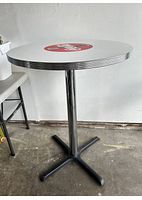Round white Coca Cola branded table with metal edges and pedestal base.