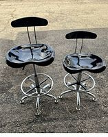 Two black drafting swivel chairs with chrome bases side by side on outdoor pavement.