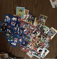 Photo showing a variety of football cards scattered on a wooden surface, featuring players in action and posed shots, mainly with blue and red bordered cards.