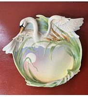 Top-down view of the detailed porcelain plate with sculpted swan and cattails on pastel background, showing condition and design.