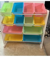 Front view of the white wooden rack with 12 colorful plastic storage bins.