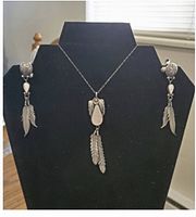 Full view of necklace and earrings on black display stand showing design and feather motifs.