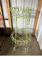 Front view of one green metal two-tier plant stand showing lattice work and curled legs.