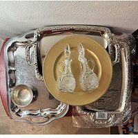 Top view showing two silver-tone serving platters, one small bowl, and two antique crystal containers on a gold-tone round tray