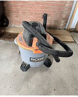 Ridgid shop vacuum with orange lid, grey container, and black hose coiled on top