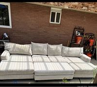 Full view of white upholstered sofa set including chaise lounge and ottoman outside under shaded area.