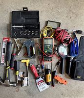 Wide view of assorted used hand tools including hammers, screwdrivers, utility knives, voltage tester, multimeter, magnifying glass, and a pack of drill bits