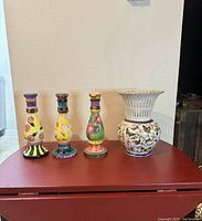 Four vases on a red surface: three tall hand-painted flower vases and one white Banko vase decorated with butterflies.