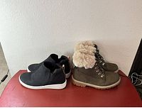 Black slip-on sneakers and grey winter boots with faux fur lining side by side on floor