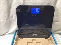 Front view of digital body weight scale powered on, showing 0.0 lb on blue backlit LCD display with A&D Medical and Bluetooth logo on front.