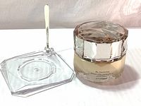 Front view of the foundation jar with clear faceted holder and gold spatula resting inside holder.