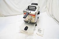 Full view of the T-Fal stainless steel deep fryer showing the unit with basket, oil storage drawer pulled out, and manuals on surface.