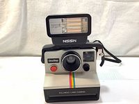Front view of Polaroid Land Camera OneStep with Nissin FTP-11 flash attached showing rainbow stripe and camera lens.