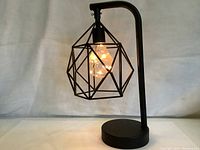Side view of black metal desk lamp with geometric wireframe shade and decorative LED filament bulb lit