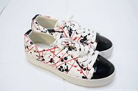 Side angled view of the sneakers showing artistic paint pattern, white laces, and gloss black toe caps.