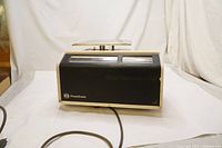 Side view of vintage Pitney Bowes postal scale showing black body, metal weighing platform on top, and attached power cord.