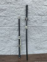 Two Japanese katana swords standing, showing full length with scabbards attached.