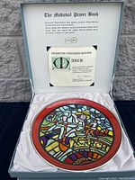 Photo of box interior lid with certificate for March plate and the March themed stained glass style plate with red border inside cushioned box.