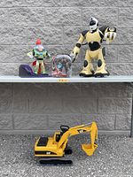 Three toys displayed outside on a shelf against a concrete block wall: Buzz Lightyear phone, Ironman robot figure, CAT excavator.