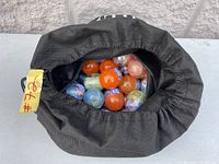 Black drawstring bag partially open showing about 20 small plastic capsule toys inside