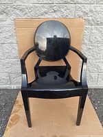 Front view of black Kartell Louis Ghost chair, showing molded translucent plastic with armrests and round back.