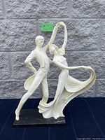 Front view of the ivory-toned dancing figurine on black marble base against stone wall background.