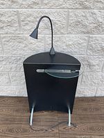 Front view of black compact desk with attached flexible lamp and glass tray folded in.