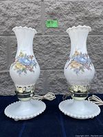 Pair of white milk glass hurricane style lamps with floral designs and round bead-edge bases.
